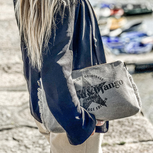 vue taille réelle, porté par mannequin, sous le bras en mode pochette. Sac pochette zazou et django, marque française. Bandoulière en cuir vegan amovible et réglable. Toile de coton doublée, fermeture zippée. Mousquetons de chaque côté. Finition en laiton. Peut se porter à la main, en bandoulière ou à l'épaule. Sac à main, trousse de maquillage/de toilette, pour la plage, porte monnaie, trousse à vernis. Parfait pour tous les jours, le boulot, la plage, les vacances, le weekend.