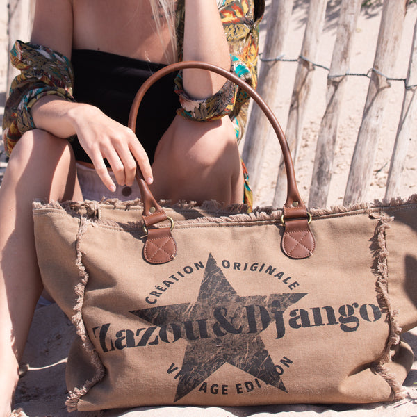 Vue taille réelle avec mannequin, dorine gaudin, porté à l'épaule, cabas weekend, couleur havane, camel, beige foncé, brun. Sac toile coton doublée, anses cuir vegan, détails laiton. Grande capacité, 30 litres. froufrous, design original, été, plage, décontracté, vintage. zazou & django, étoile, marque française.