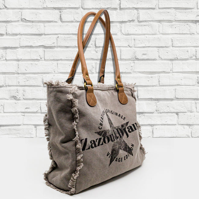 vue côté sac mini cabas quotidien couleur taupe, gris,. Toile doublée en coton, détails laitons et cuir vegan. Style décontracté, vintage, froufrous, plage, été. Design original zazou & django.